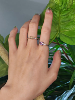 woman wearing prehnite and lavender rings with a pink gemstone against a green leafy background